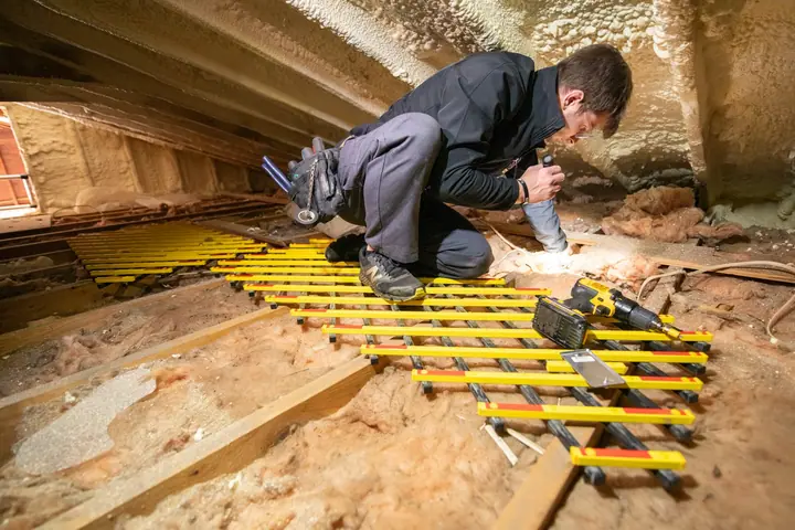 Technician kneeling on boards over attic insulation